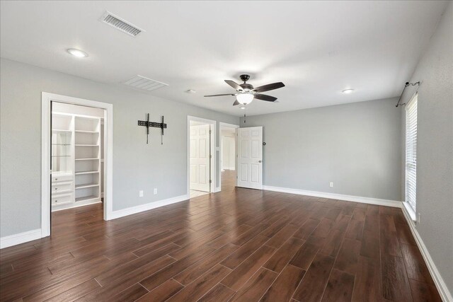 empty room with dark wood finished floors, visible vents, a ceiling fan, and baseboards