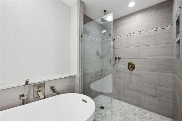 bathroom with a soaking tub and tiled shower