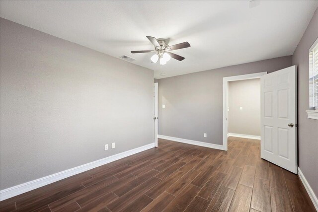 spare room featuring dark wood-style floors, visible vents, a ceiling fan, and baseboards