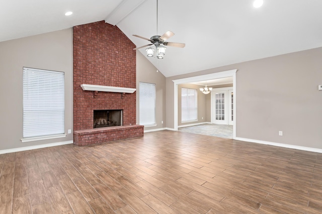 unfurnished living room with a brick fireplace, beamed ceiling, wood finished floors, and ceiling fan with notable chandelier