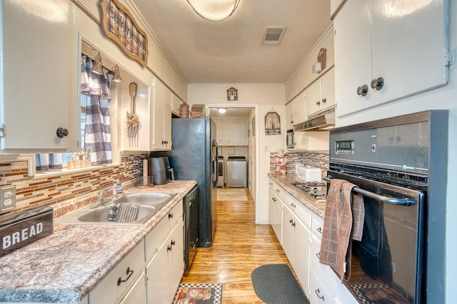 kitchen with sink, white cabinets, independent washer and dryer, black appliances, and light wood-type flooring