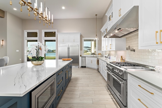 kitchen with blue cabinetry, built in appliances, white cabinets, a center island, and hanging light fixtures