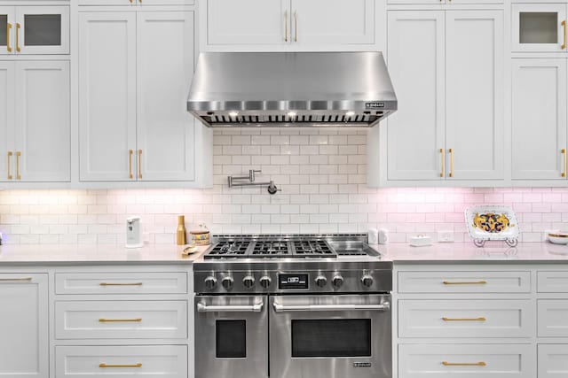 kitchen featuring white cabinets, decorative backsplash, range with two ovens, and wall chimney range hood