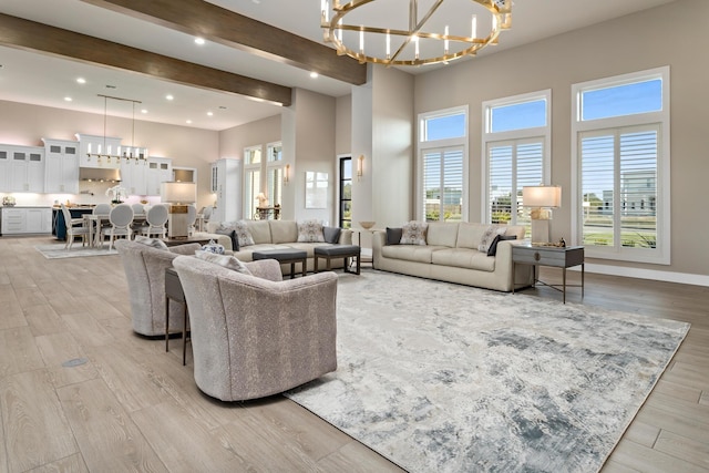 living room with beam ceiling, light wood-type flooring, a high ceiling, and an inviting chandelier