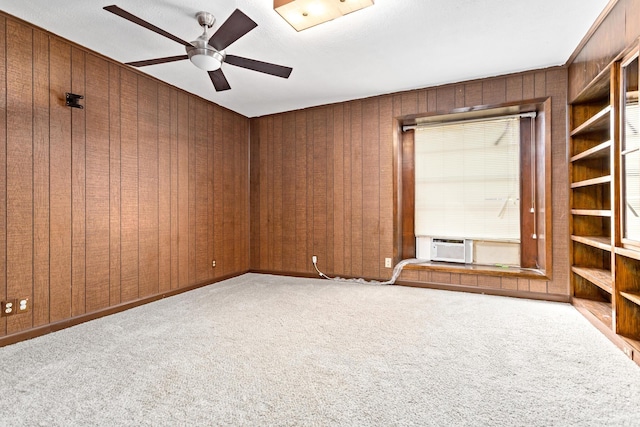 carpeted empty room featuring built in shelves, cooling unit, ceiling fan, and wooden walls