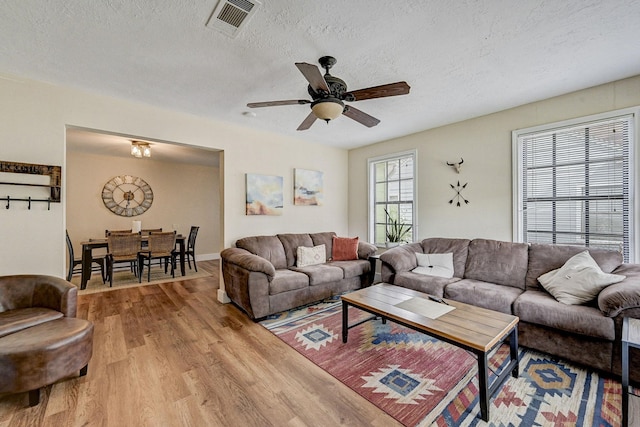 living room featuring ceiling fan, light wood-type flooring, and a textured ceiling