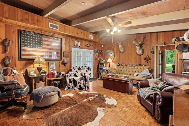 living area featuring beamed ceiling, wooden walls, visible vents, and ceiling fan