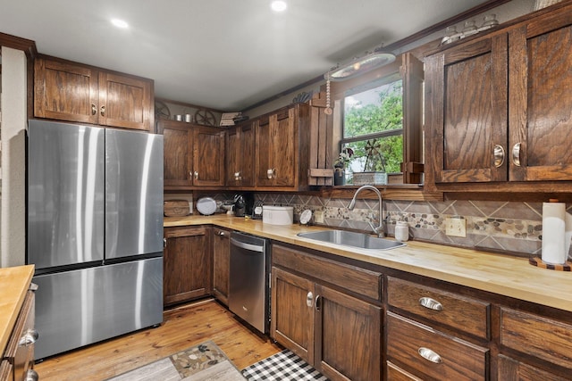 kitchen featuring a sink, wooden counters, decorative backsplash, light wood-style floors, and appliances with stainless steel finishes