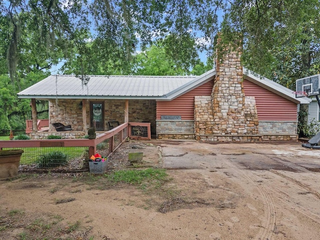 back of house with faux log siding, a porch, stone siding, a chimney, and metal roof