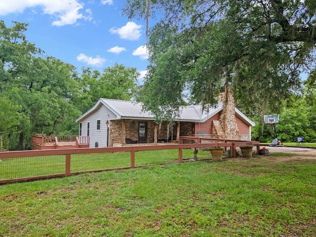back of house featuring stone siding, a chimney, metal roof, a lawn, and a deck