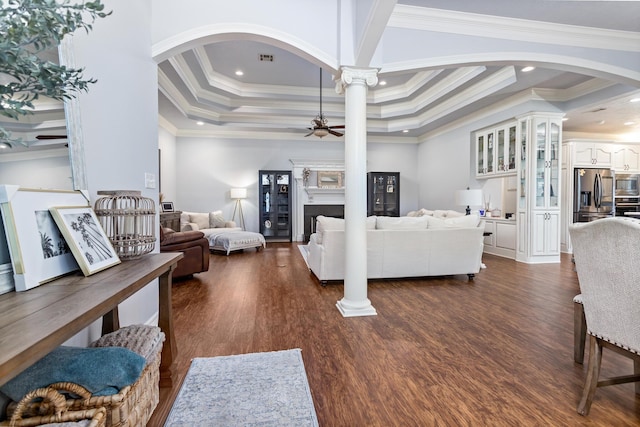 living room featuring a raised ceiling, ornate columns, crown molding, and ceiling fan