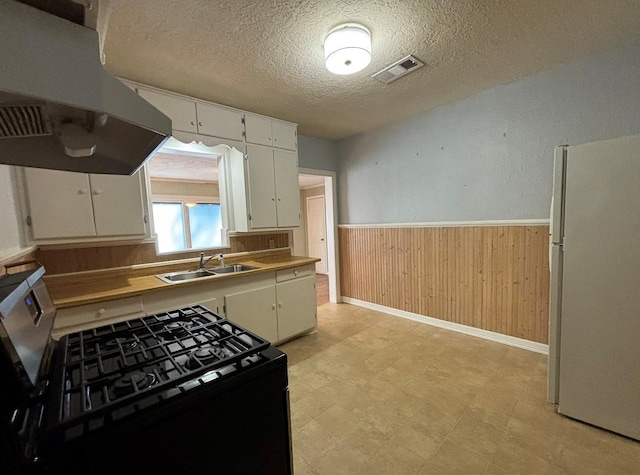 kitchen featuring visible vents, a sink, freestanding refrigerator, under cabinet range hood, and gas range oven