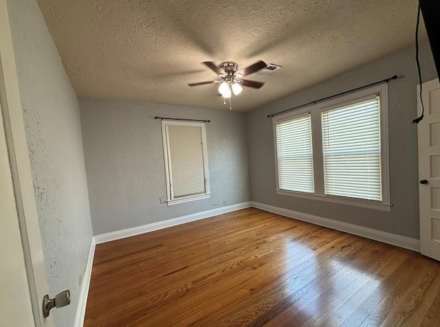 spare room with ceiling fan, a textured ceiling, visible vents, wood finished floors, and baseboards