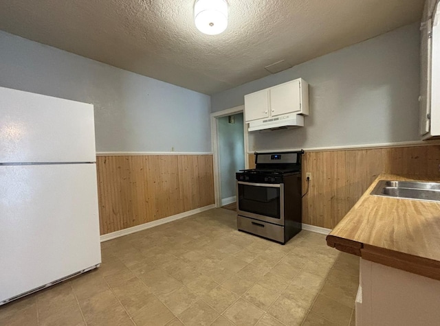 kitchen featuring stainless steel range with gas stovetop, freestanding refrigerator, under cabinet range hood, and wood walls