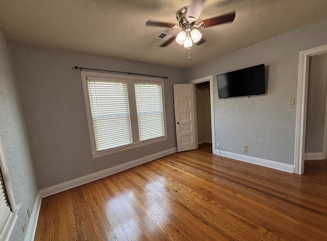 unfurnished bedroom featuring ceiling fan, a textured ceiling, visible vents, wood finished floors, and baseboards