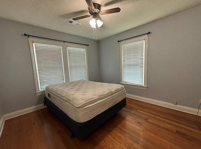 bedroom featuring a textured ceiling, baseboards, visible vents, and wood finished floors