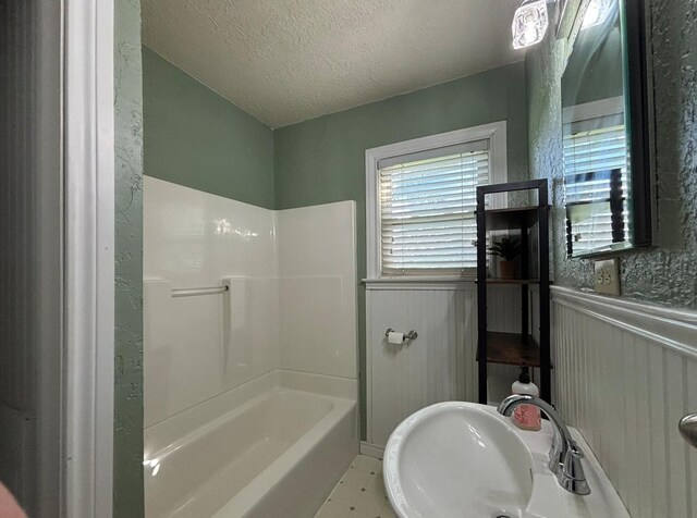 full bathroom with a sink, wainscoting, a textured ceiling, and shower / bathtub combination