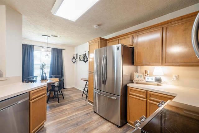 kitchen with light wood-type flooring, visible vents, appliances with stainless steel finishes, light countertops, and decorative light fixtures