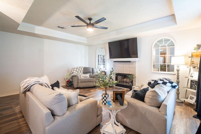 living area featuring visible vents, a ceiling fan, a fireplace, a tray ceiling, and wood finished floors