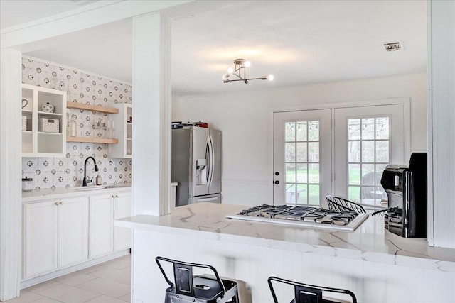 kitchen featuring visible vents, a sink, stainless steel fridge, white gas cooktop, and light stone countertops