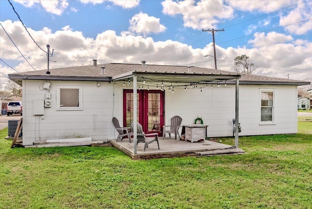 rear view of property featuring french doors, a lawn, roof with shingles, and a patio area