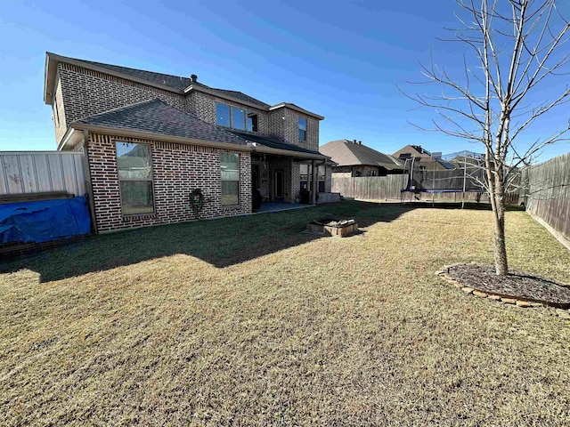 view of yard featuring a trampoline, a fenced backyard, and an outdoor fire pit