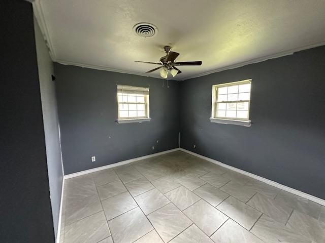 spare room with baseboards, ceiling fan, visible vents, and a healthy amount of sunlight