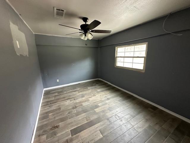 empty room with a ceiling fan, wood finished floors, baseboards, and visible vents