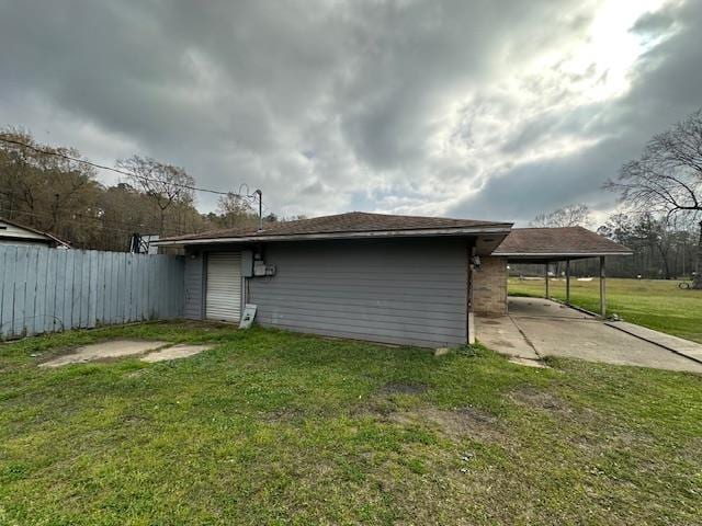 back of house with driveway, a carport, fence, and a lawn