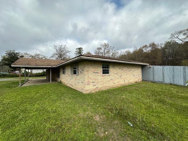 view of side of home with a lawn, an attached carport, fence, and brick siding