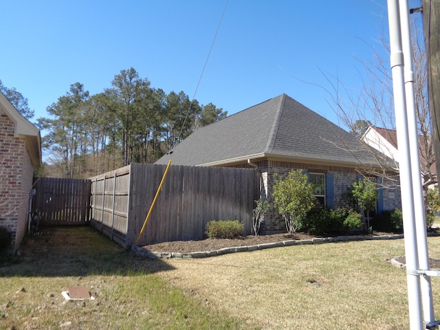 view of side of property with a yard, fence, brick siding, and a shingled roof