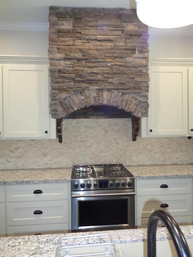 kitchen with light stone counters, decorative backsplash, white cabinetry, crown molding, and stainless steel gas stove