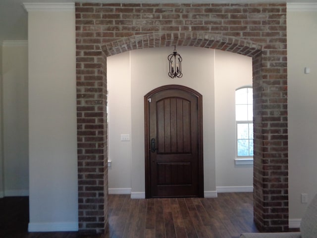 foyer with baseboards, arched walkways, wood finished floors, and crown molding