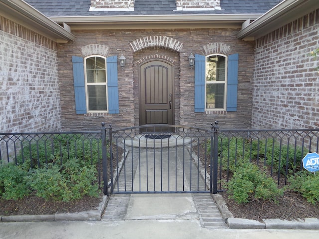 property entrance featuring a gate, a shingled roof, and fence