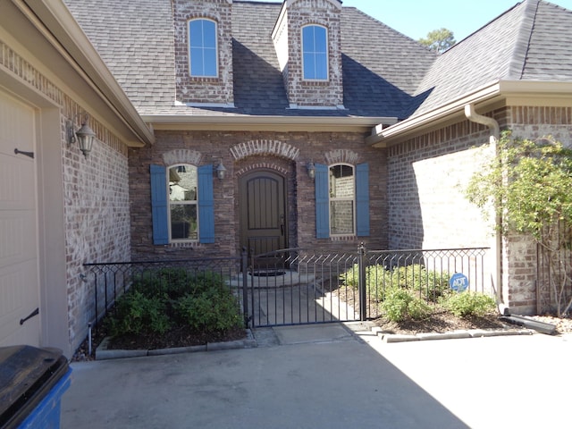 property entrance featuring brick siding, a gate, roof with shingles, and fence