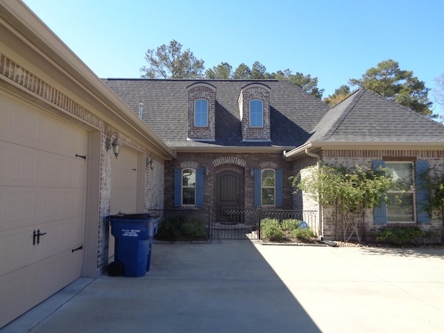 exterior space with brick siding, an attached garage, driveway, and a shingled roof