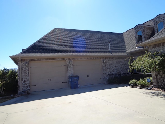 view of side of home featuring a garage, brick siding, driveway, and a shingled roof