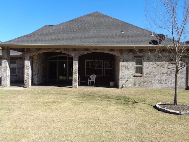 back of property with brick siding, a patio area, a yard, and roof with shingles