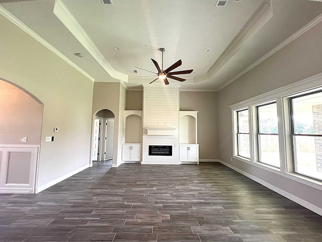 unfurnished living room with ornamental molding, a large fireplace, a tray ceiling, ceiling fan, and a high ceiling