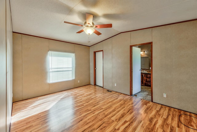unfurnished bedroom with crown molding, light hardwood / wood-style flooring, ensuite bathroom, a textured ceiling, and vaulted ceiling