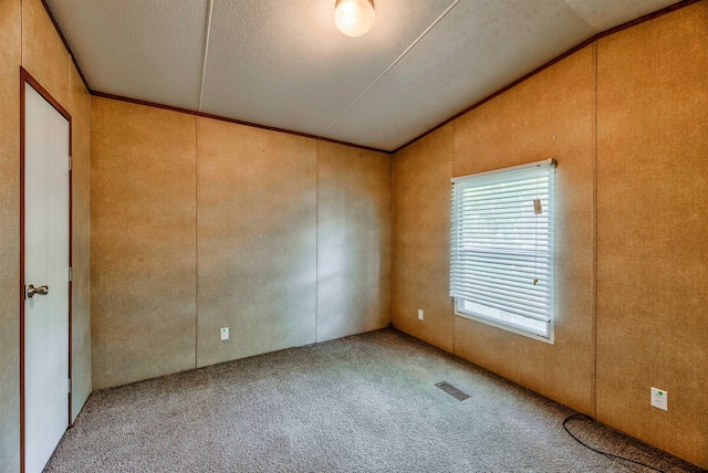 spare room featuring vaulted ceiling, carpet flooring, a textured ceiling, and crown molding