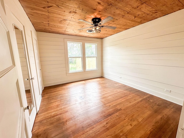 empty room featuring wood walls, ceiling fan, wood ceiling, and light wood-type flooring