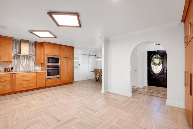 kitchen with a barn door, wall chimney exhaust hood, stainless steel appliances, and ornamental molding