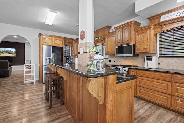 503 Country Wood Cir, Sour Lake, TX 77659 - kitchen with appliances with stainless steel finishes, arched walkways, dark wood finished floors, decorative backsplash, and a kitchen bar
