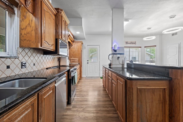 503 Country Wood Cir, Sour Lake, TX 77659 - kitchen with appliances with stainless steel finishes, wood finished floors, brown cabinetry, backsplash, and dark stone counters