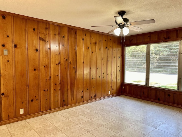 empty room with a textured ceiling, ceiling fan, and wooden walls