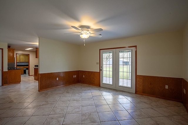 tiled spare room featuring ceiling fan and wood walls