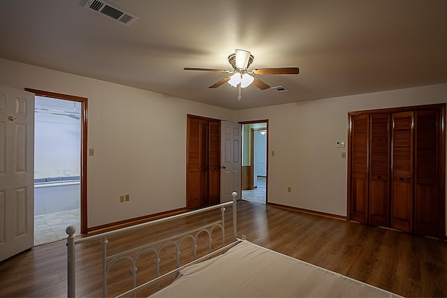 unfurnished bedroom with dark wood-type flooring, two closets, and ceiling fan