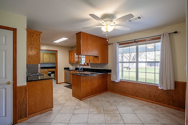 kitchen featuring light tile patterned flooring, stainless steel dishwasher, wood walls, and kitchen peninsula