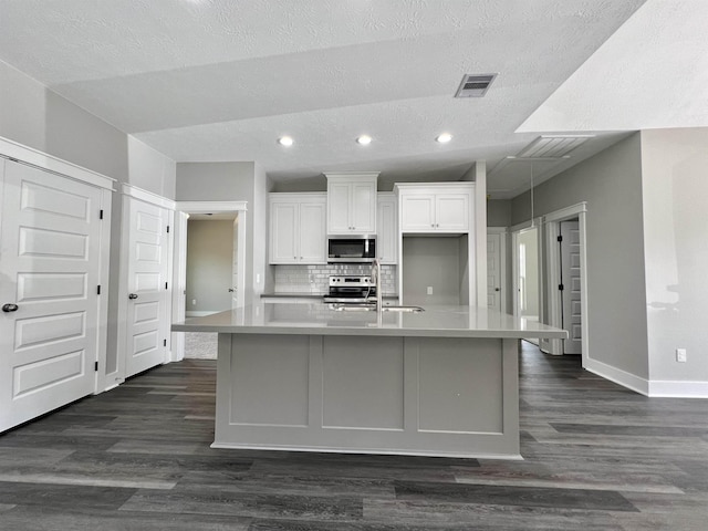 kitchen featuring lofted ceiling, tasteful backsplash, appliances with stainless steel finishes, a kitchen island with sink, and white cabinets